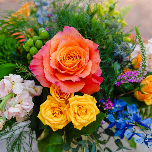 Bouquet of colorful flowers including orange, yellow, and blue roses with greenery.