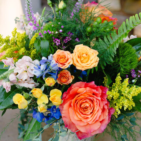 Colorful flower arrangement with roses and various other flowers in a decorative vase.
