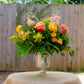 Floral arrangement in a glass vase on a table outdoors with a wooden fence in the background.
