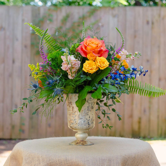 Colorful floral arrangement in a decorative vase on a table outdoors.