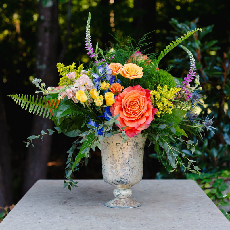 Colorful floral arrangement in a glass vase on a stone pedestal with a blurred green background