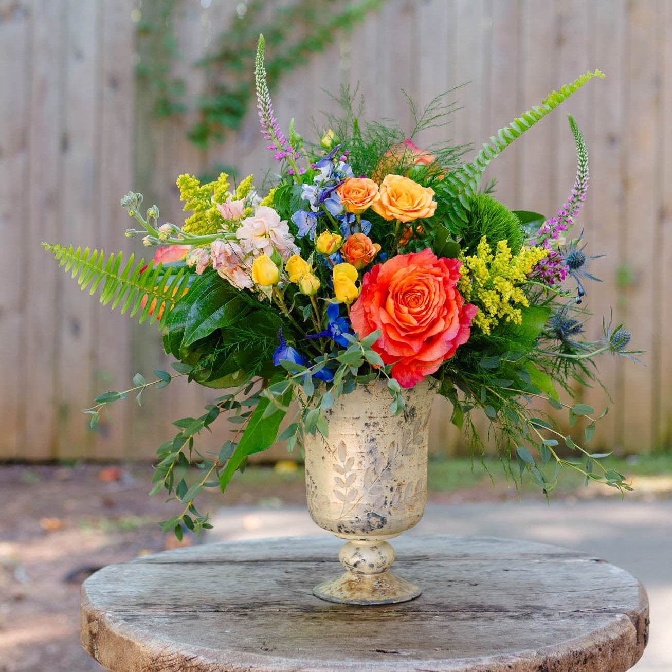 Colorful floral arrangement in a decorative vase on a wooden table outdoors.
