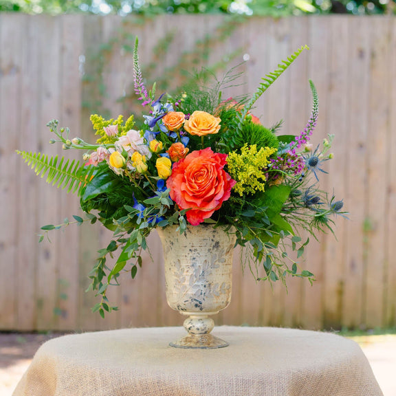 Colorful floral arrangement in a decorative vase on a table outdoors.
