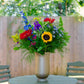 Colorful flower arrangement in a vase on a round table outdoors.