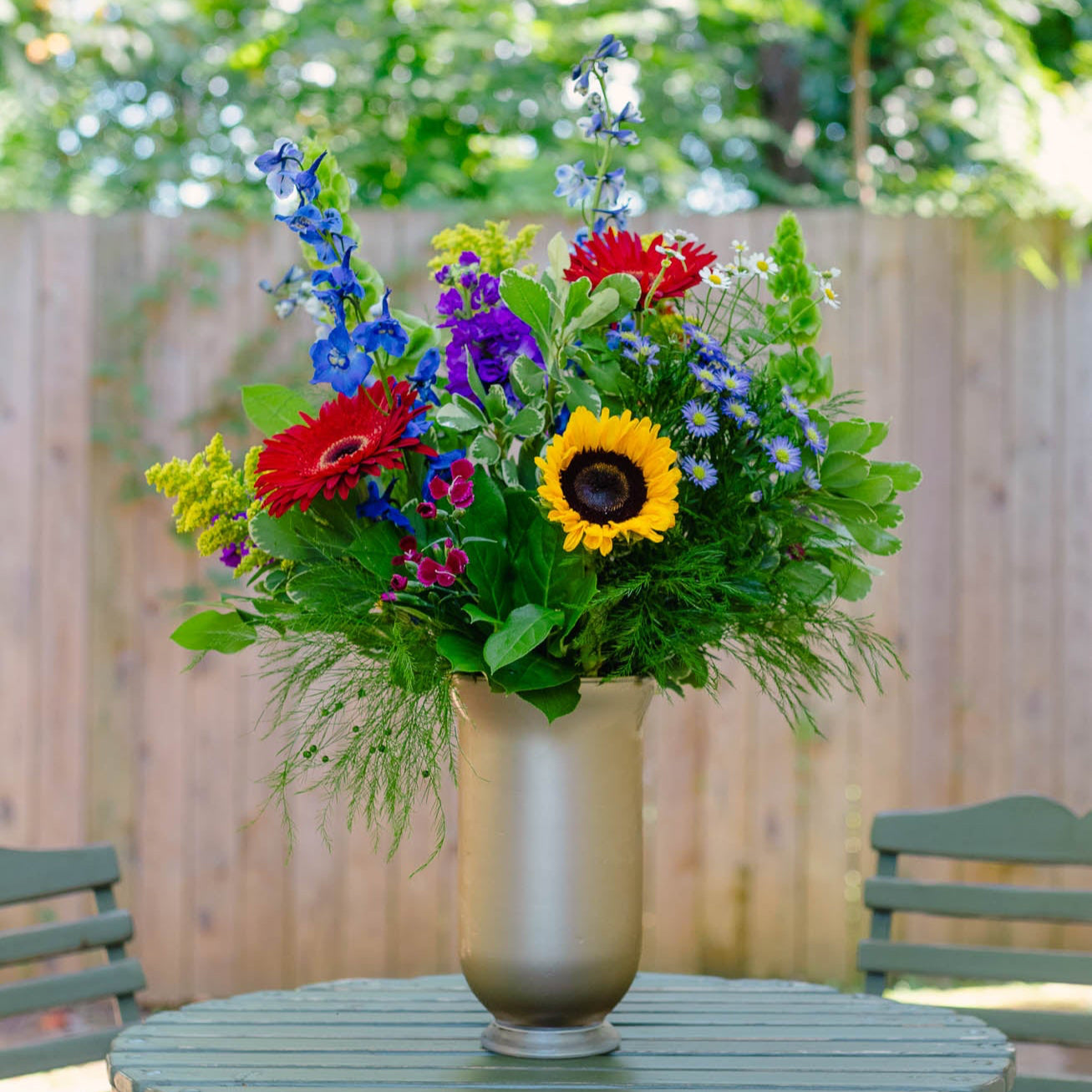 Colorful flower arrangement in a vase on a round table outdoors.