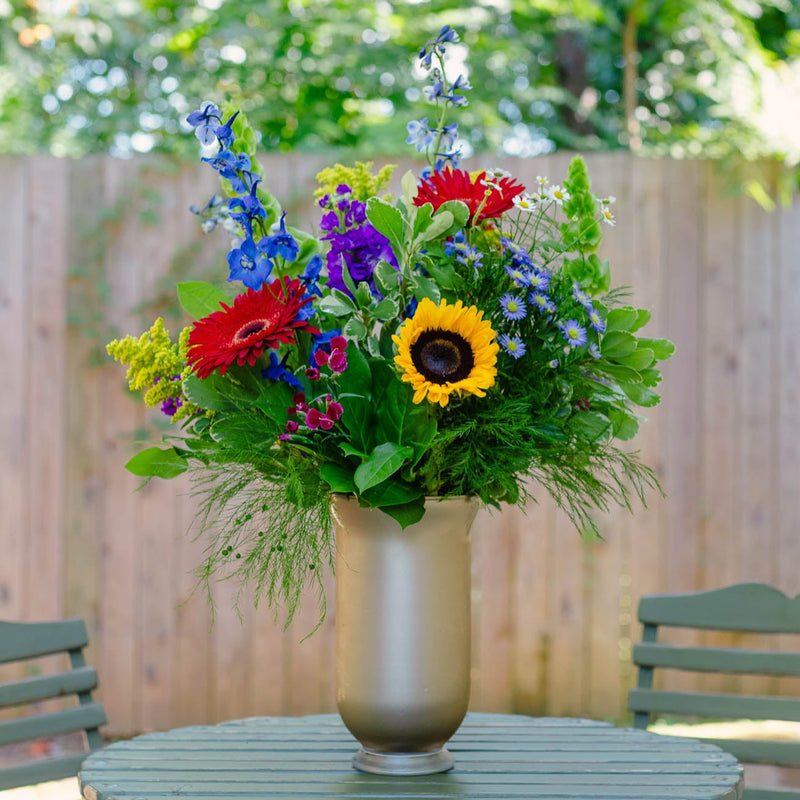 Colorful flower arrangement in a vase on a round table outdoors.