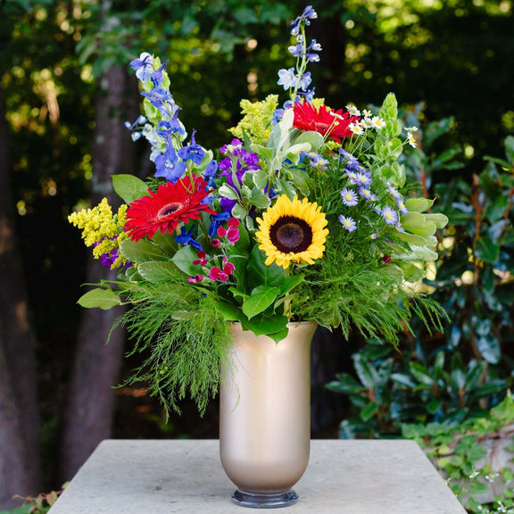 Colorful flower arrangement in a vase on a stone pedestal with greenery in the background