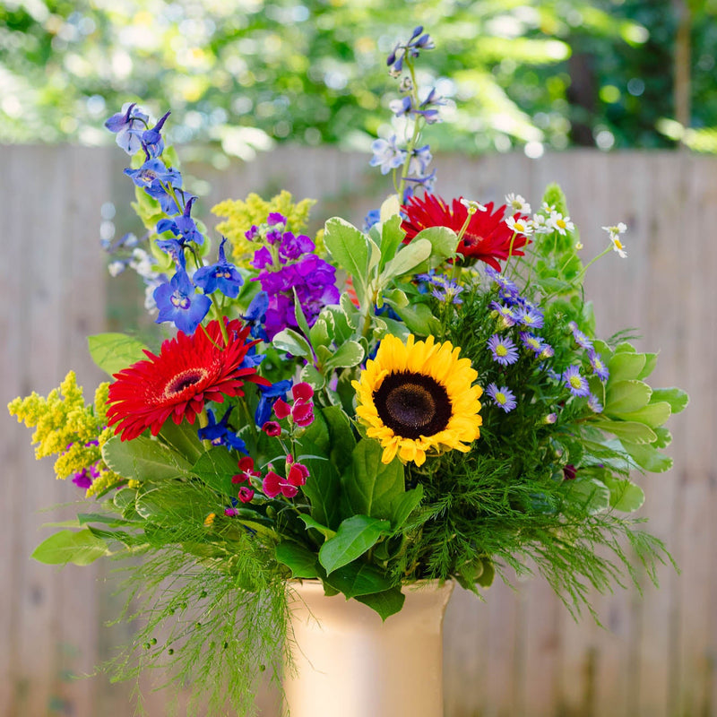 Colorful bouquet of flowers in a vase on a wooden table outdoors.